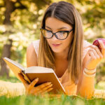 outside portrait of young beautiful woman with apple reading book in park