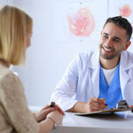 Handsome doctor is talking with young female patient and making notes while sitting in his office